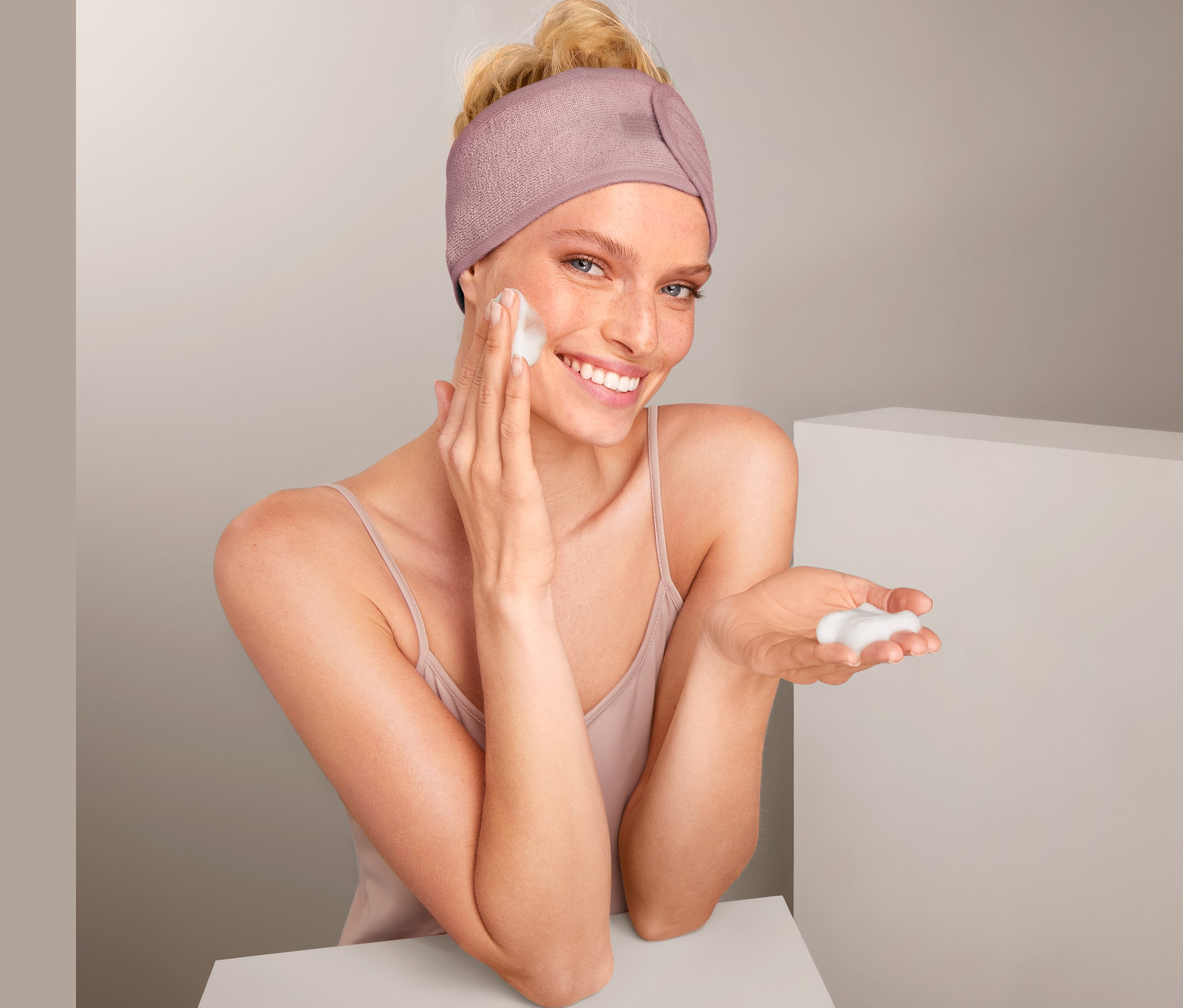 Frau trägt 2 Kosmetik-Stirnbänder und trägt Schaum auf ihr Gesicht auf.