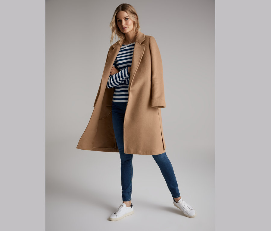 Frau trägt einen camel Mantel aus weicher Wollmischung, ein blau-weiß gestreiftes T-Shirt, Jeans und Turnschuhe.