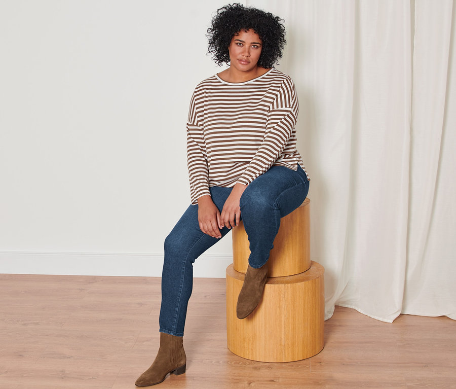 Eine Frau sitzt auf Holzwürfeln und trägt eine Stiefelette aus Veloursleder, eine Slim-Denim »Fit Emma«, dark blue denim und ein Gestreiftes Langarmshirt, beige.