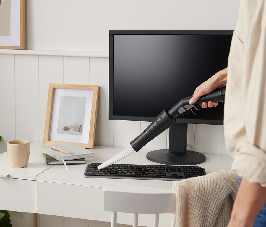 Frau benutzt Staubsaugeraufsatz auf Computertastatur auf weißem Schreibtisch.