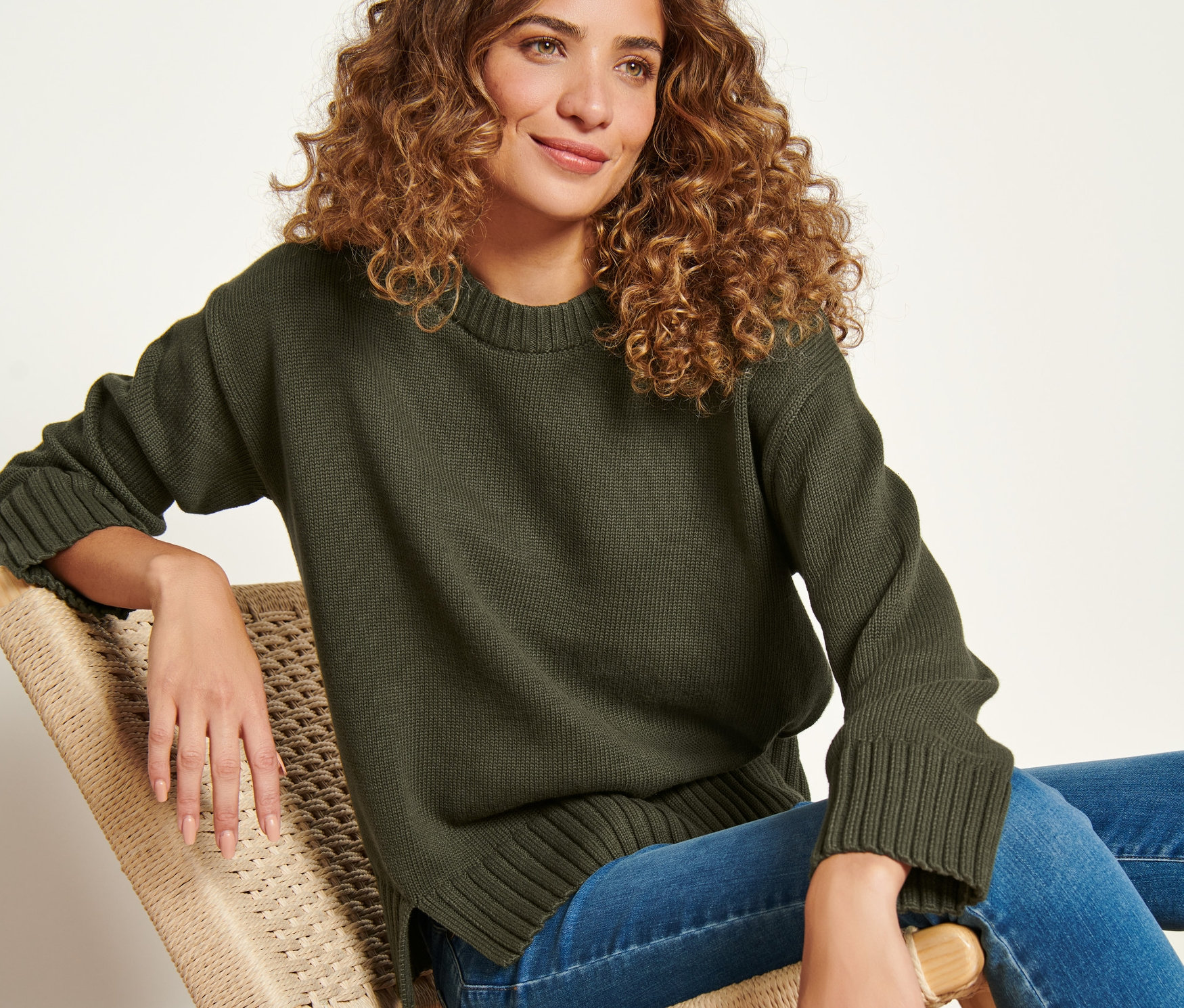 Frau sitzt im Stuhl und trägt einen Strickpullover mit Saumschlitz.