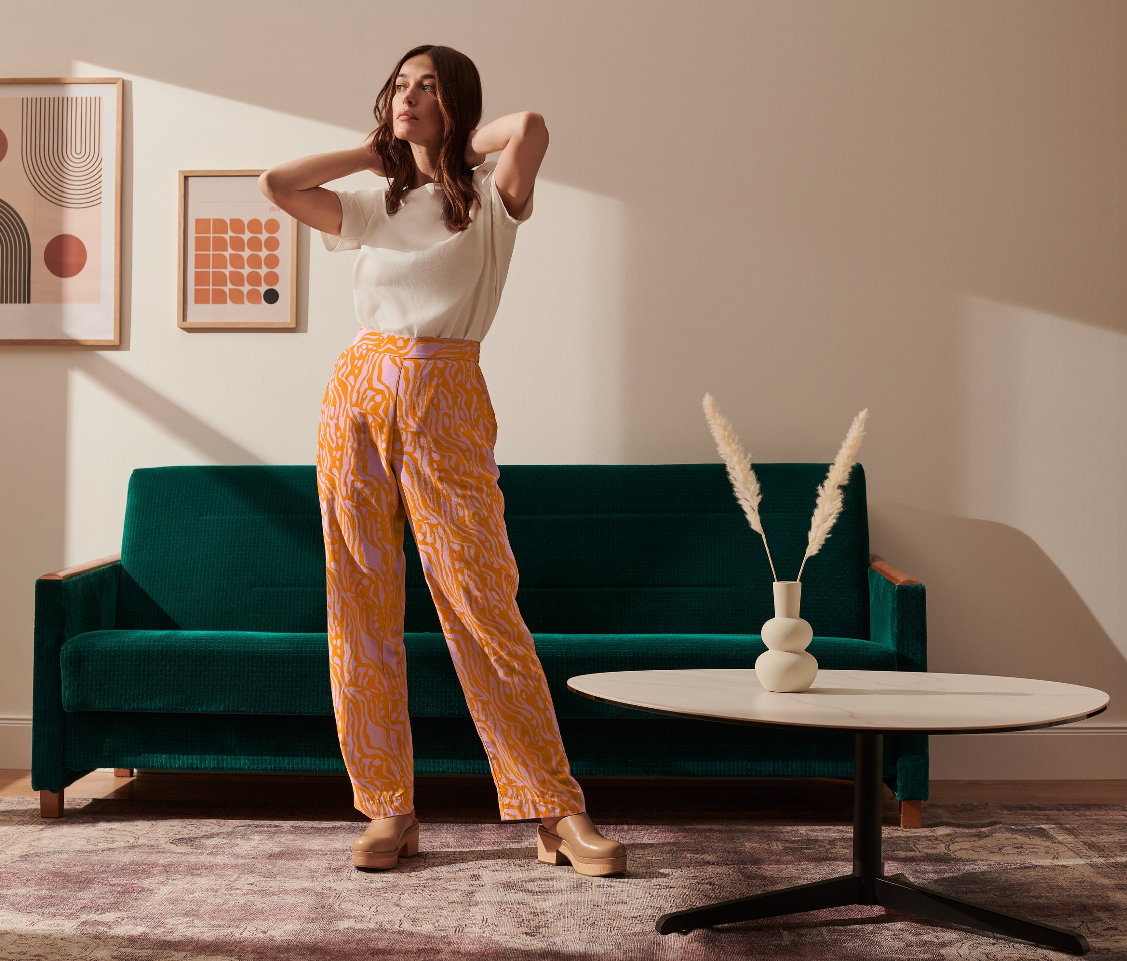 Eine Frau posiert in einer orange-lila Webhose neben einem grünen Sofa.