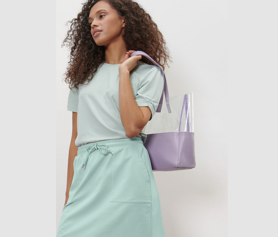 Frau posiert in mintfarbenem Sweatrock und lila Handtasche.