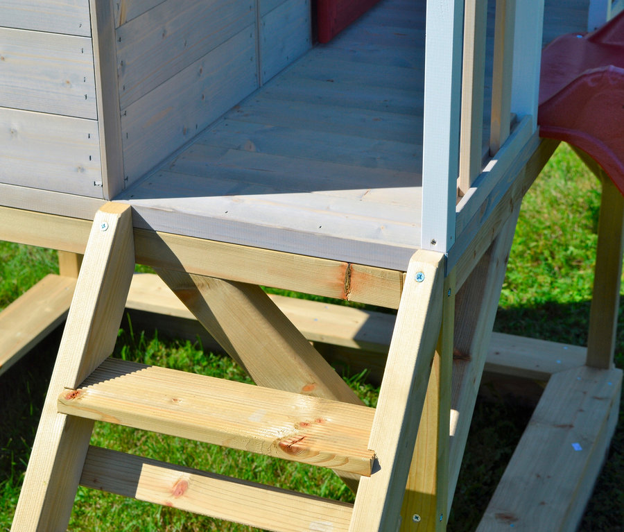 Detailansicht des Wendi Spielhaus »Alpaka« aus Holz mit Leiter und Rutsche auf einer grünen Wiese.