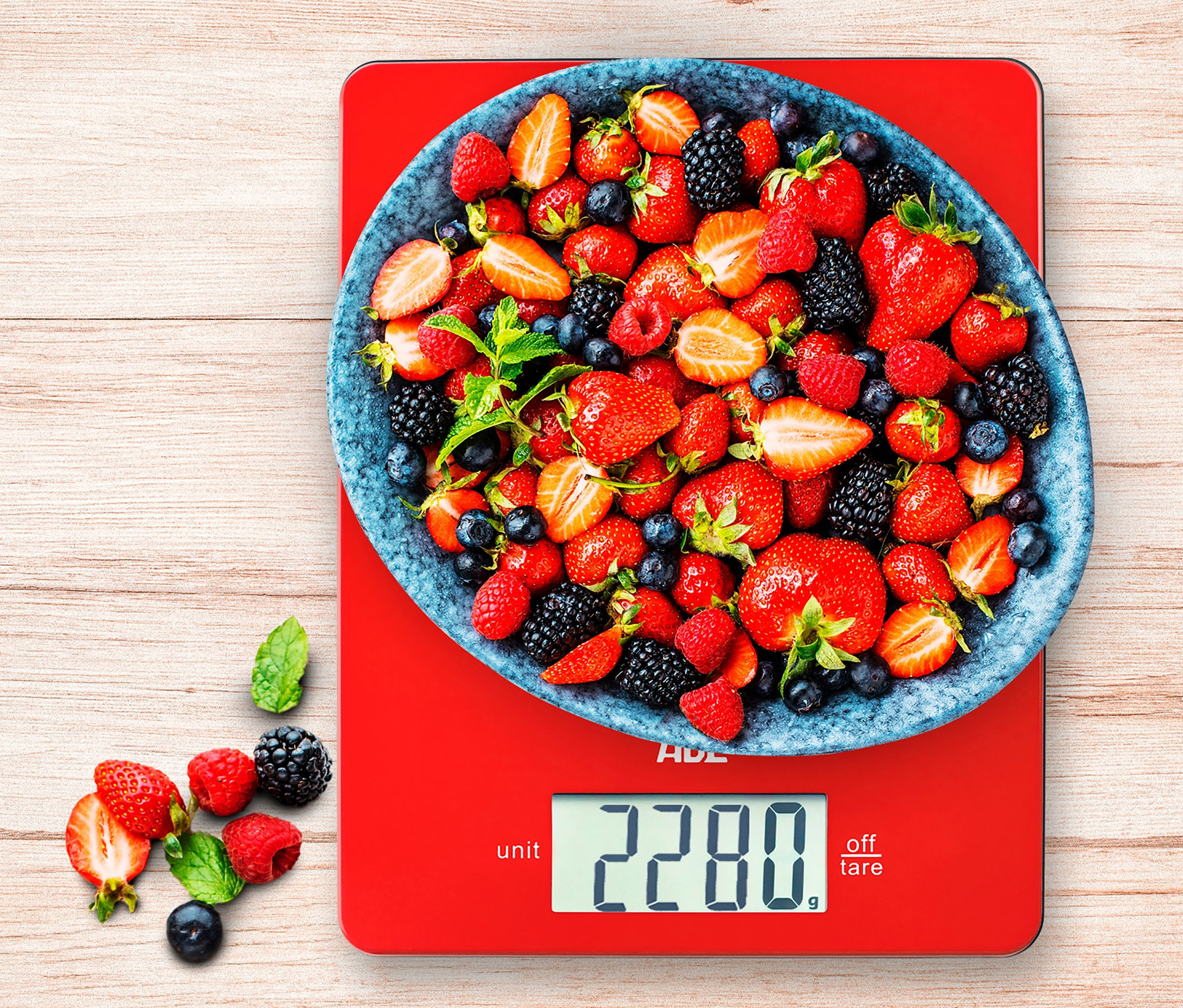 Eine Schüssel mit Erdbeeren, Himbeeren und Blaubeeren steht auf der roten digitalen Küchenwaage ADE »Leonie«.
