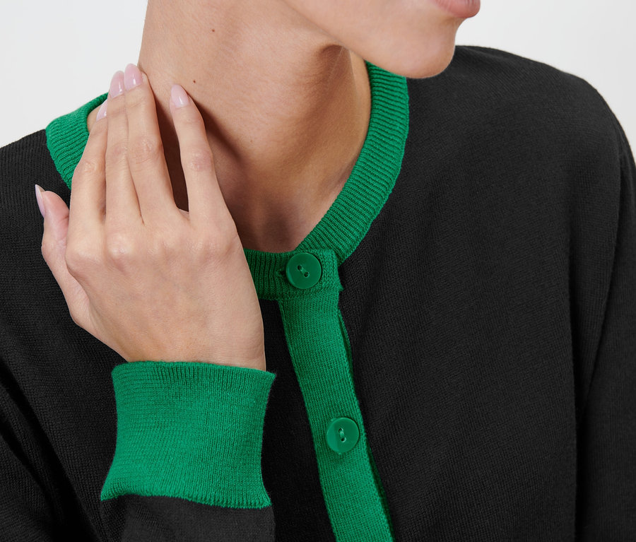 Detailaufnahme einer Frau, die einen schwarzen Feinstrick-Cardigan mit grünen Akzenten trägt.