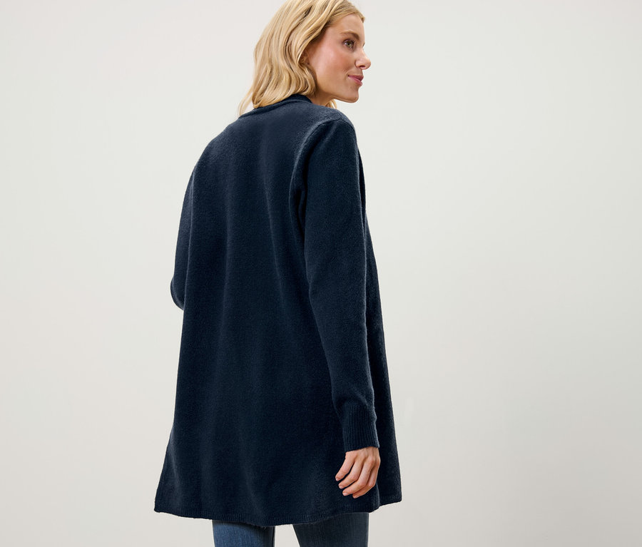 Blonde Frau mit Jeans und offenem Longcardigan blickt nach rechts.