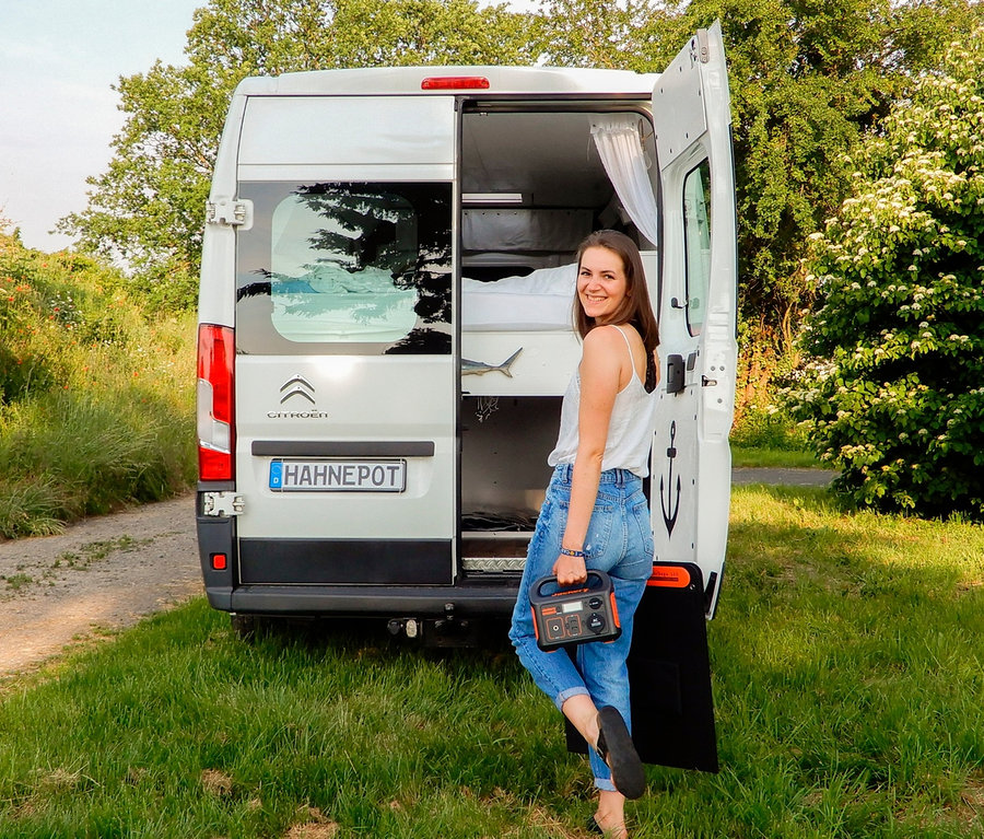 Frau steht an der offenen Tür eines weißen Lieferwagens und hält einen Jackery Explorer 240.