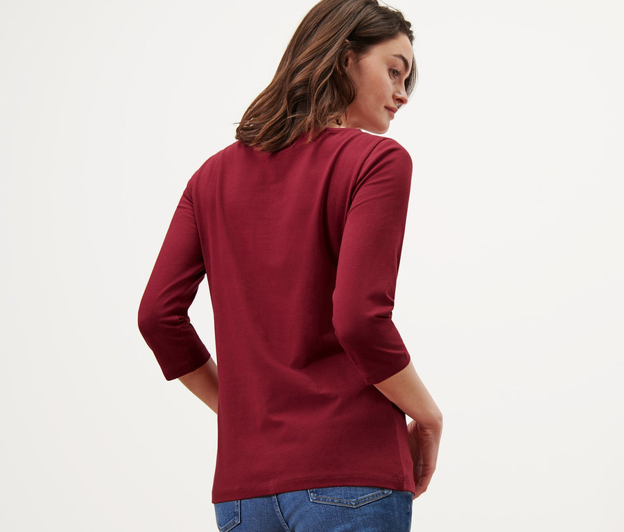 Frau posiert von hinten mit einem bordeauxroten Shirt mit 3/4-Arm und Jeans.