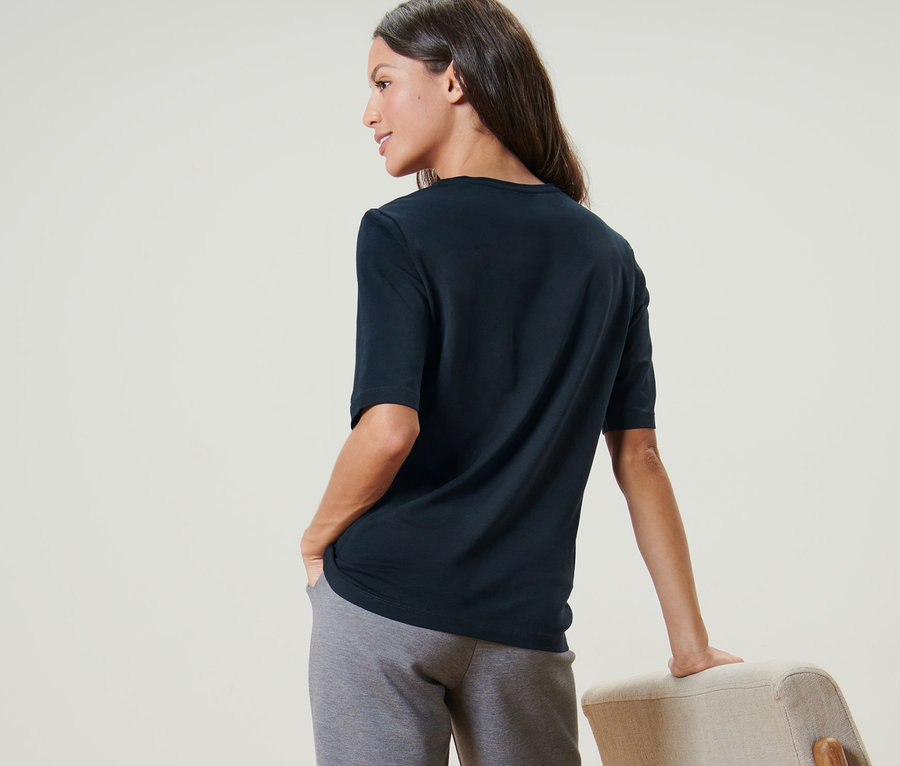 Frau von hinten mit dunkelblauem Basic Halbarmshirt und grauer Hose.