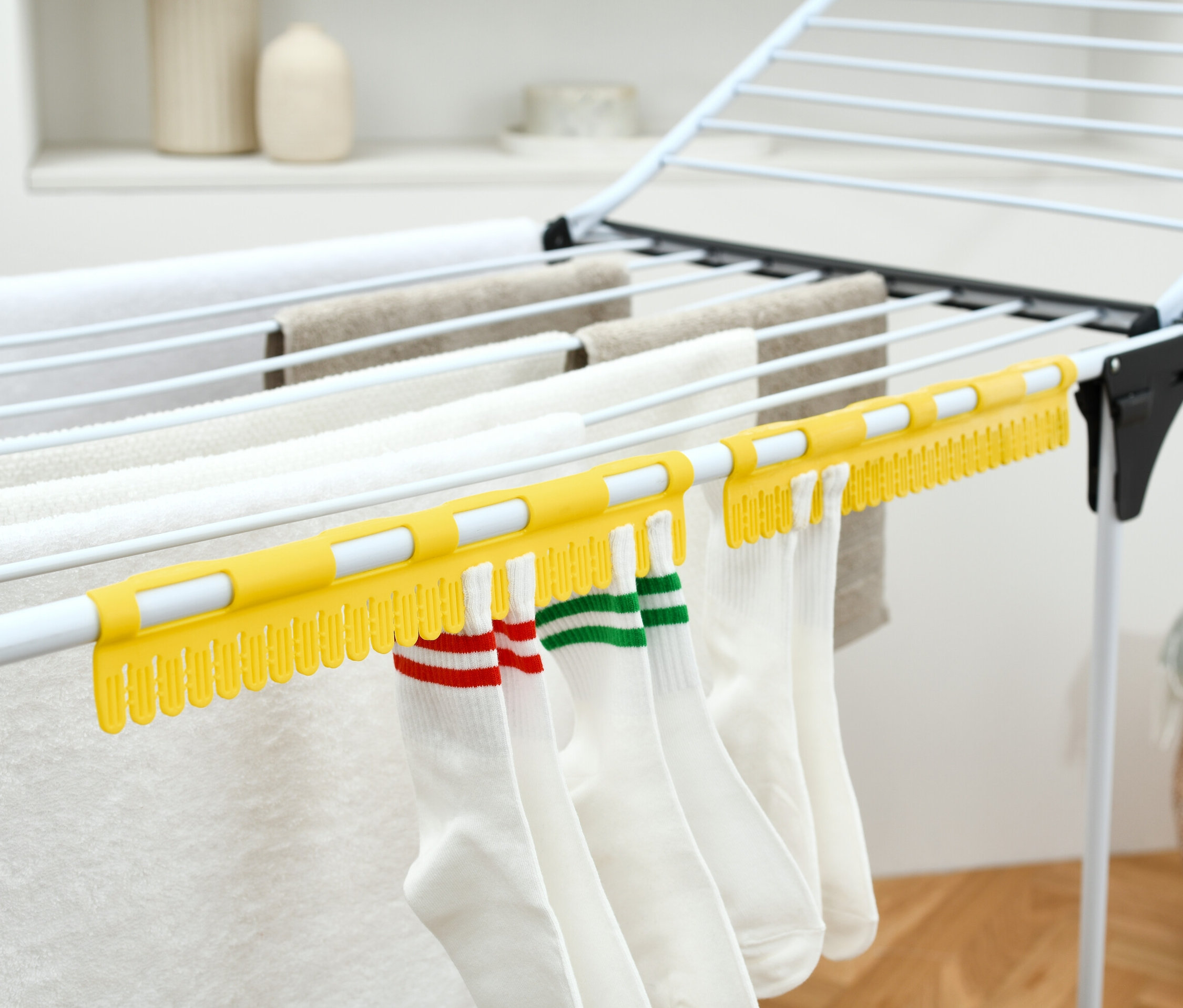 Weiße Socken hängen an einem gelben 2 Sockentrockner auf einem Wäscheständer.
