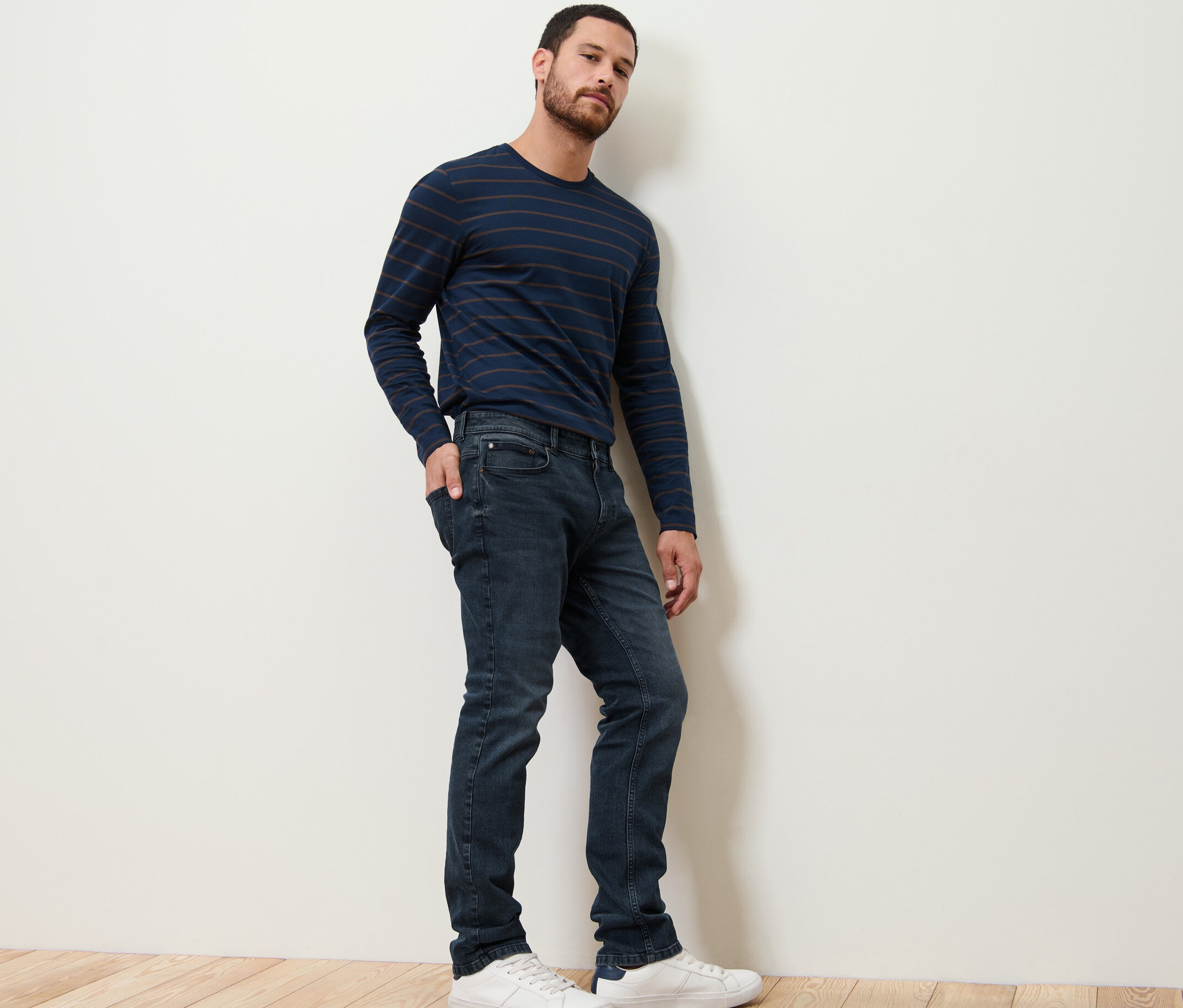 Mann posiert in Jeans und gestreiftem Shirt.