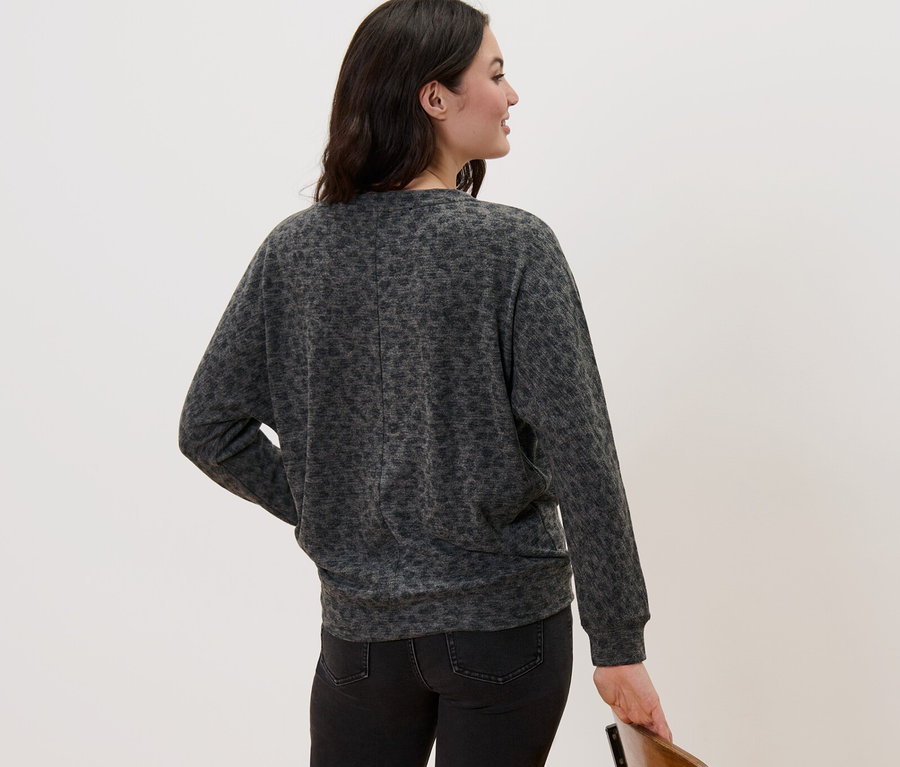 Frau steht mit dem Rücken und trägt ein bedrucktes Fledermausshirt und schwarze Jeans.