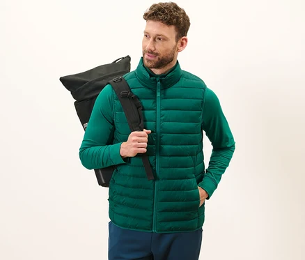 Mann trägt eine grüne verstaubare Steppweste und einen schwarzen Rucksack.