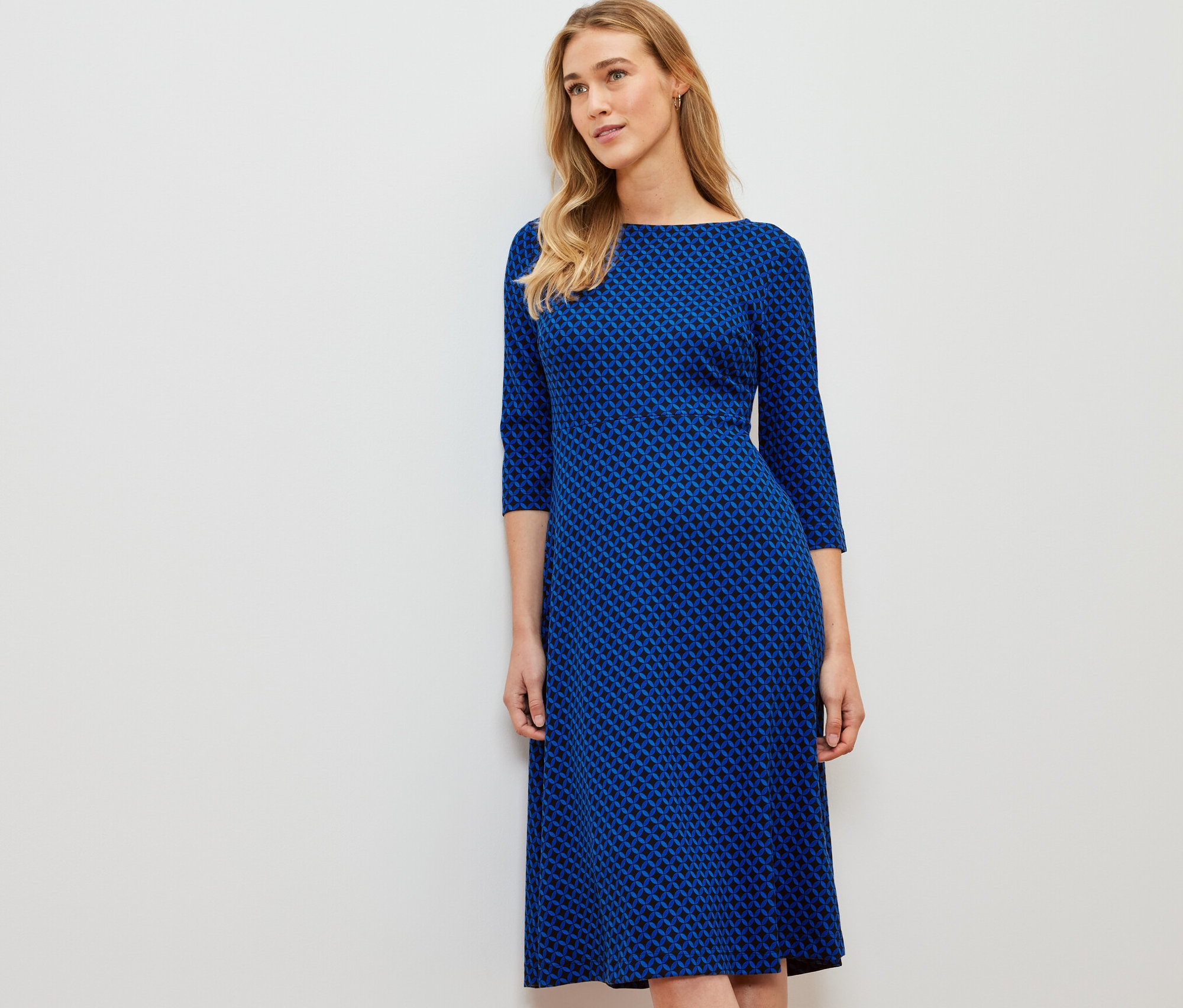 Eine Frau steht und trägt ein bedrucktes Jerseykleid.