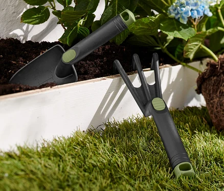 Teil eines Gartenwerkzeug-Sets liegt auf Gras neben einer blauen Hortensie.