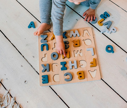 Ein Kind spielt mit einem ABC-Puzzle »Caspar« auf einem weißen Holzboden.
