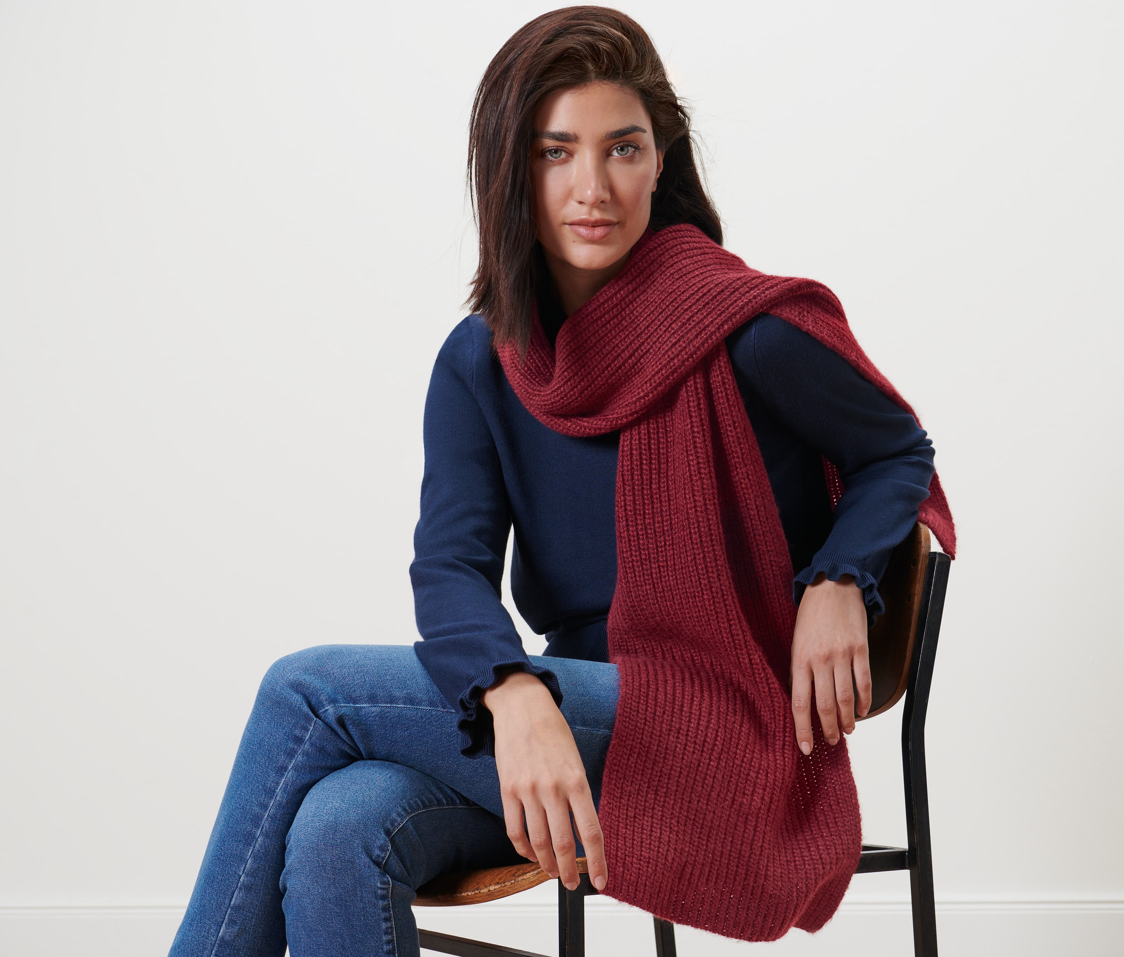 Frau sitzt auf einem Stuhl und trägt einen Strickschal mit Wolle.