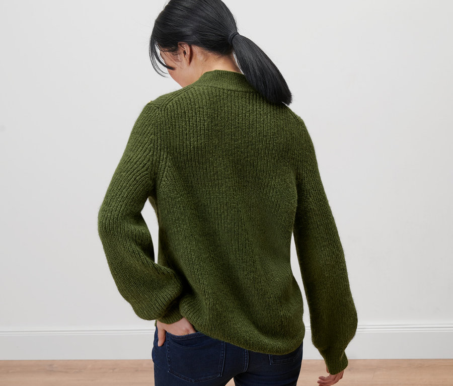 Frau von hinten trägt einen Grobstrickpullover mit Knöpfen und Jeans.