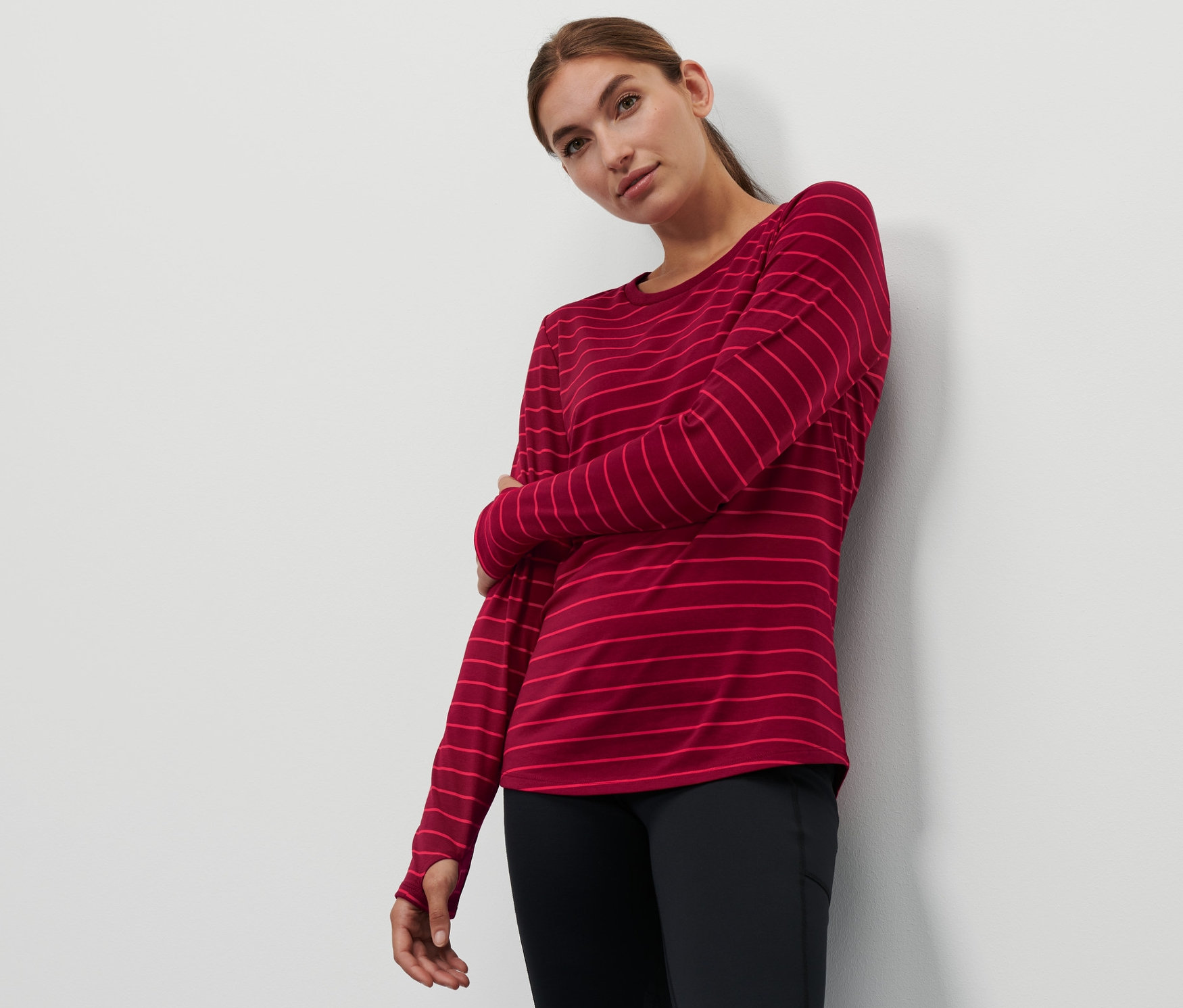 Frau posiert in einem weinrot gestreiften Langarm-Sportshirt und schwarzen Leggings.