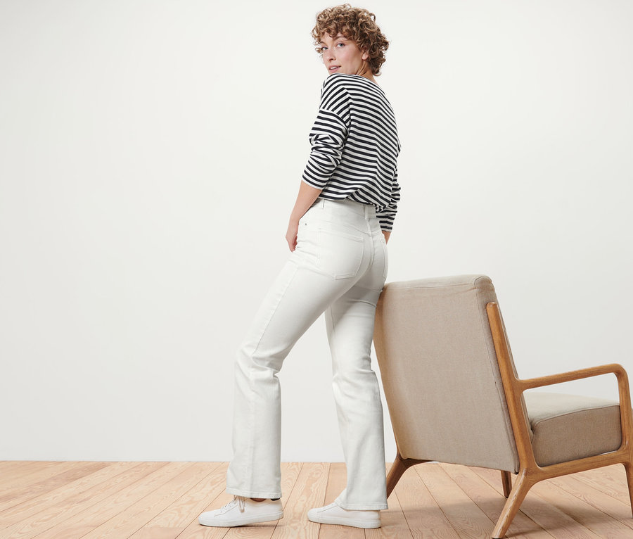 Frau blickt über die Schulter und posiert in cremeweißen Bootcut Jeans – Fit »Lou«.