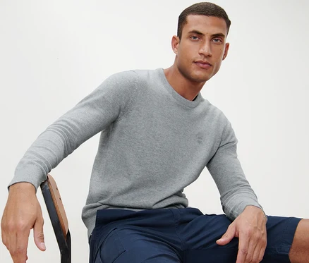 Mann sitzt auf einem Stuhl und trägt einen grauen Pullover mit Rundhalsausschnitt.