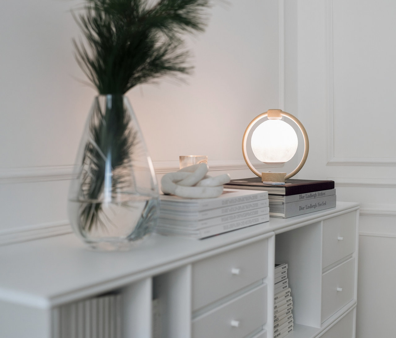 Schwebender LED-Bluetooth®-Lautsprecher »Mond« steht auf Büchern auf einem weißen Schrank neben einer Vase mit Grünzeug.
