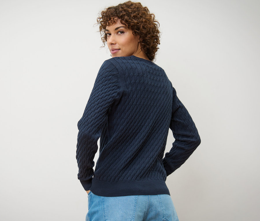 Frau blickt über die Schulter und trägt einen dunkelblauen Zopfstrickpullover.