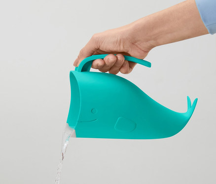 Eine Hand hält einen blaugrünen Kinder-Haarwaschbecher in Walform, aus dem Wasser fließt.