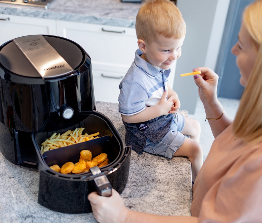 Frau gibt Jungen Pommes, der neben der Steba Heißluftfritteuse sitzt.