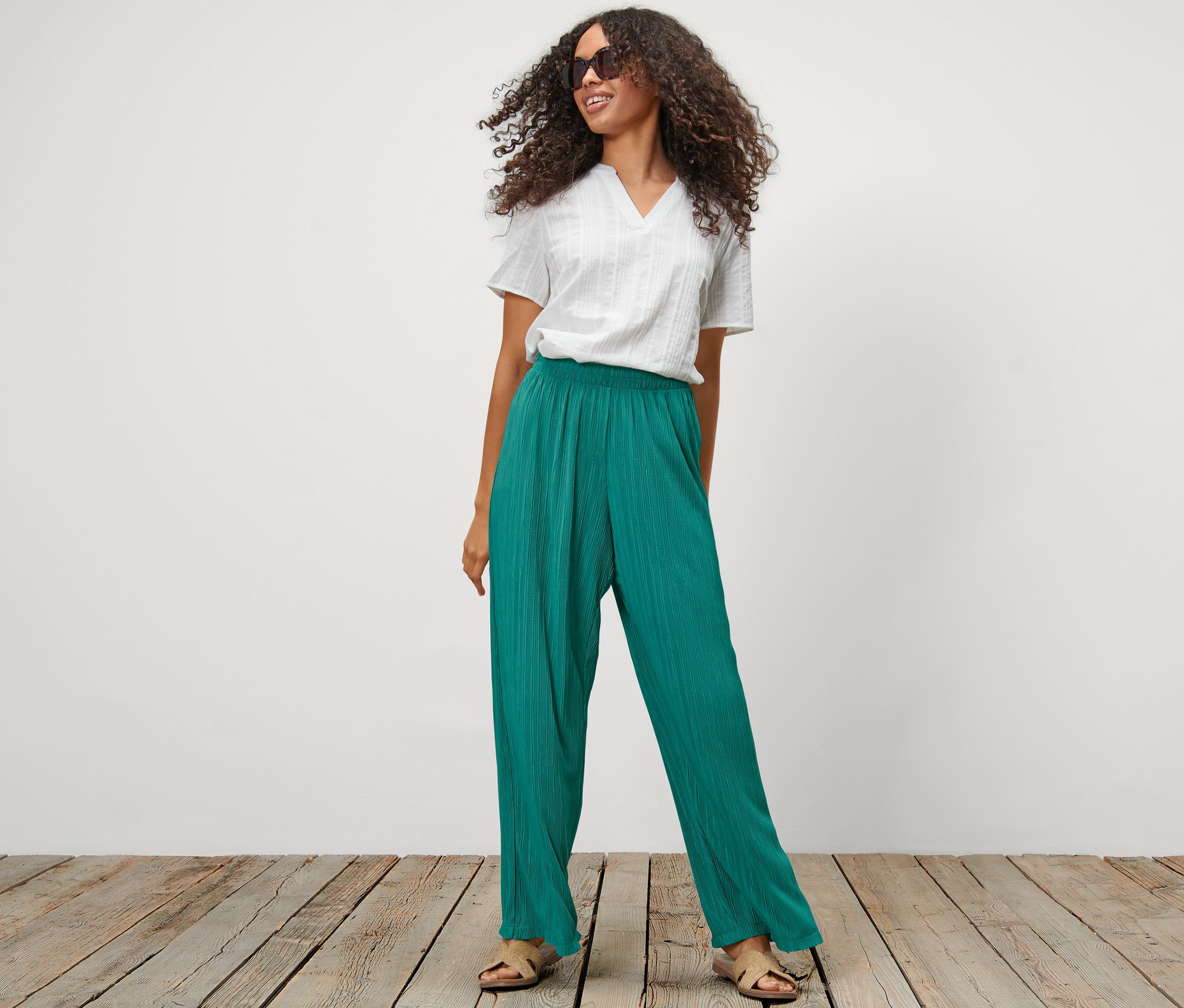 Frau posiert in petrolgrüner Plisseehose und weißem Oberteil.
