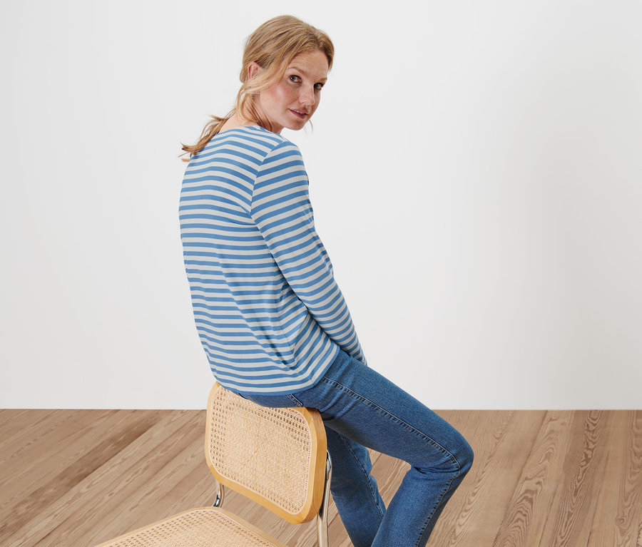 Frau sitzt auf einem Stuhl und trägt ein gestreiftes Langarmshirt und Jeans.