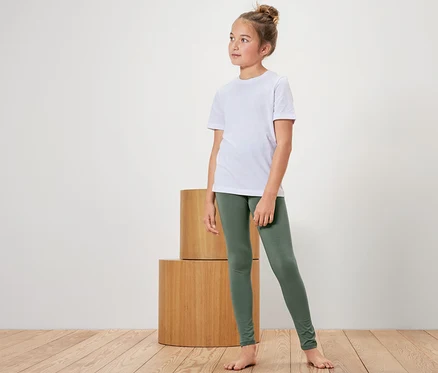 Ein Mädchen in einem weißen T-Shirt und grünen Leggings steht neben Holzzylindern.