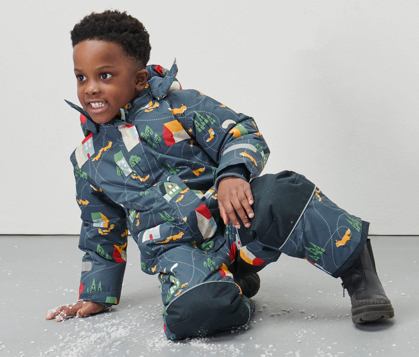 Junge liegt im Schneeanzug mit Fuchs-Alloverprint auf dem Boden.