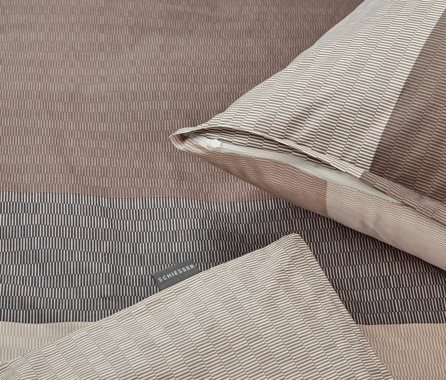 Detail einer braun gestreiften Bettwäsche und eines Kissens mit Reißverschluss.