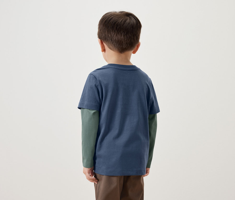 Rückseite eines kleinen Jungen in einem blauen T-Shirt mit langen grünen Ärmeln und braunen Hosen.