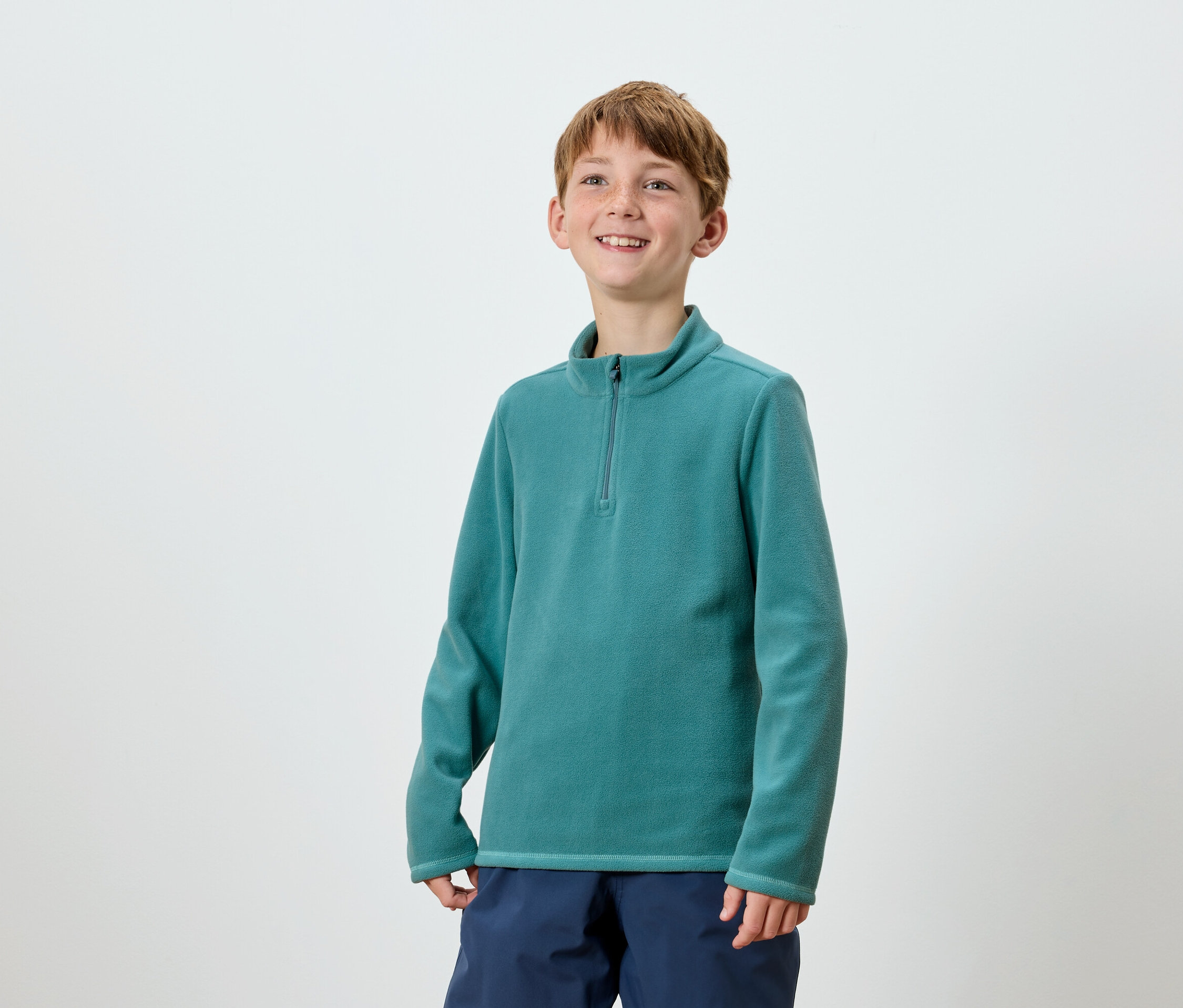 Lächelnder Junge posiert in türkisfarbenem Fleecepullover mit Reißverschluss und dunkelblauer Hose.