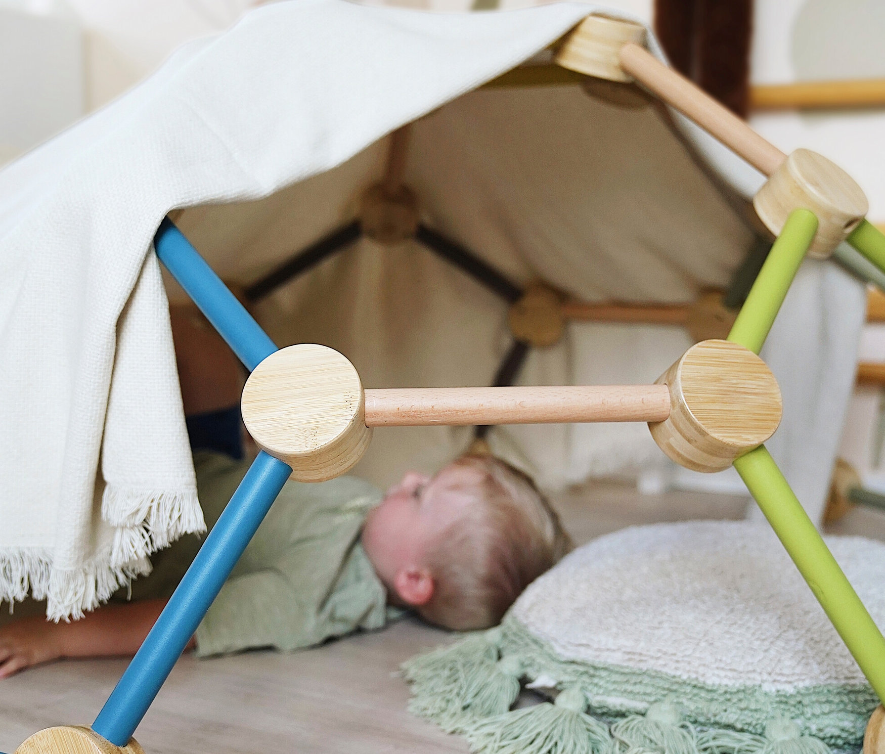 Ein Junge liegt unter der mit einem Tuch bedeckten small foot Kletterkuppel »Adventure«.