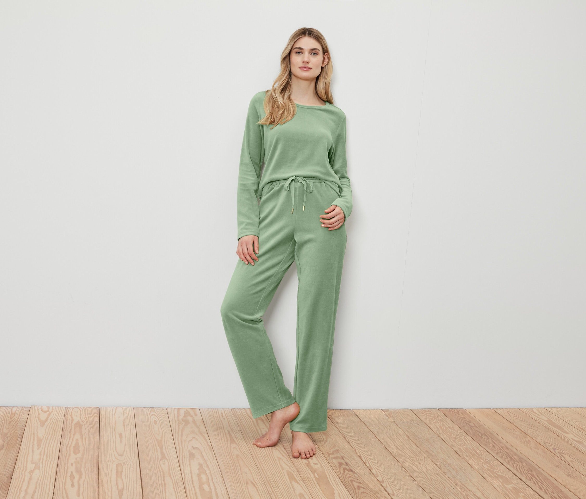 Frau posiert in einem grünen Pullover und einer Hose.