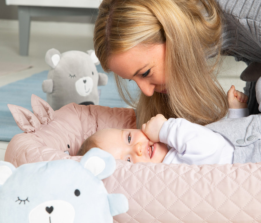 Eine Mutter schaut auf ein lachendes Baby, das in einer rosa Roba Babylounge liegt.