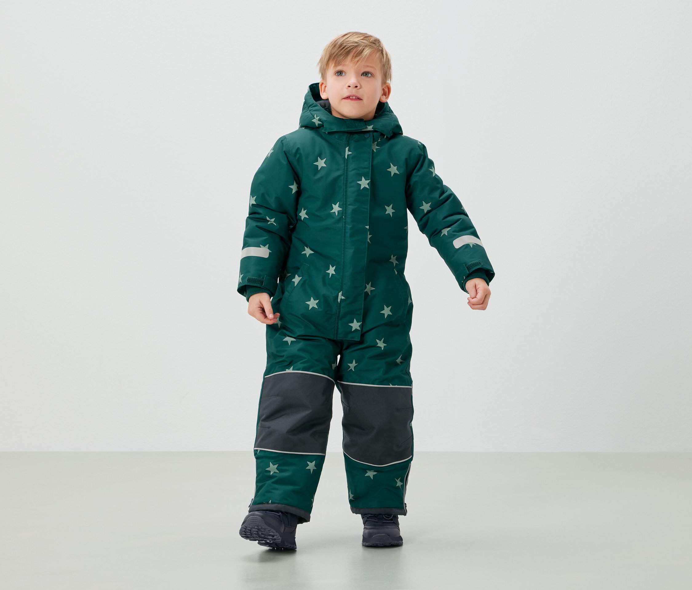 Junge steht in grünem Overall mit Sternen.