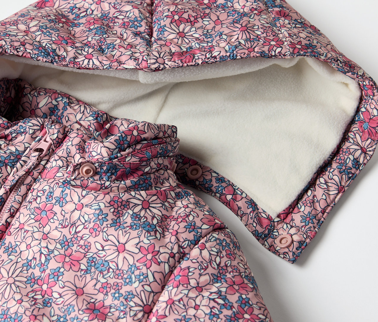 Detailaufnahme eines Baby-Winteroveralls mit Blumenmuster und Kapuze.