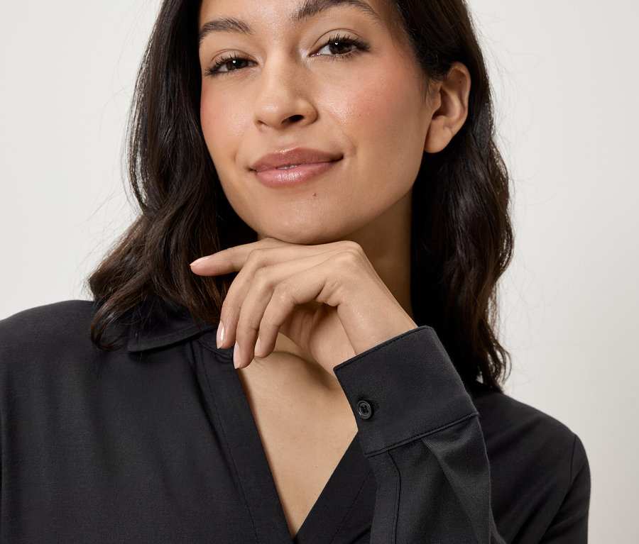 Porträt einer Frau mit braunen Haaren, die ein schwarzes Hemd trägt und ihr Kinn auf ihre Hand stützt.