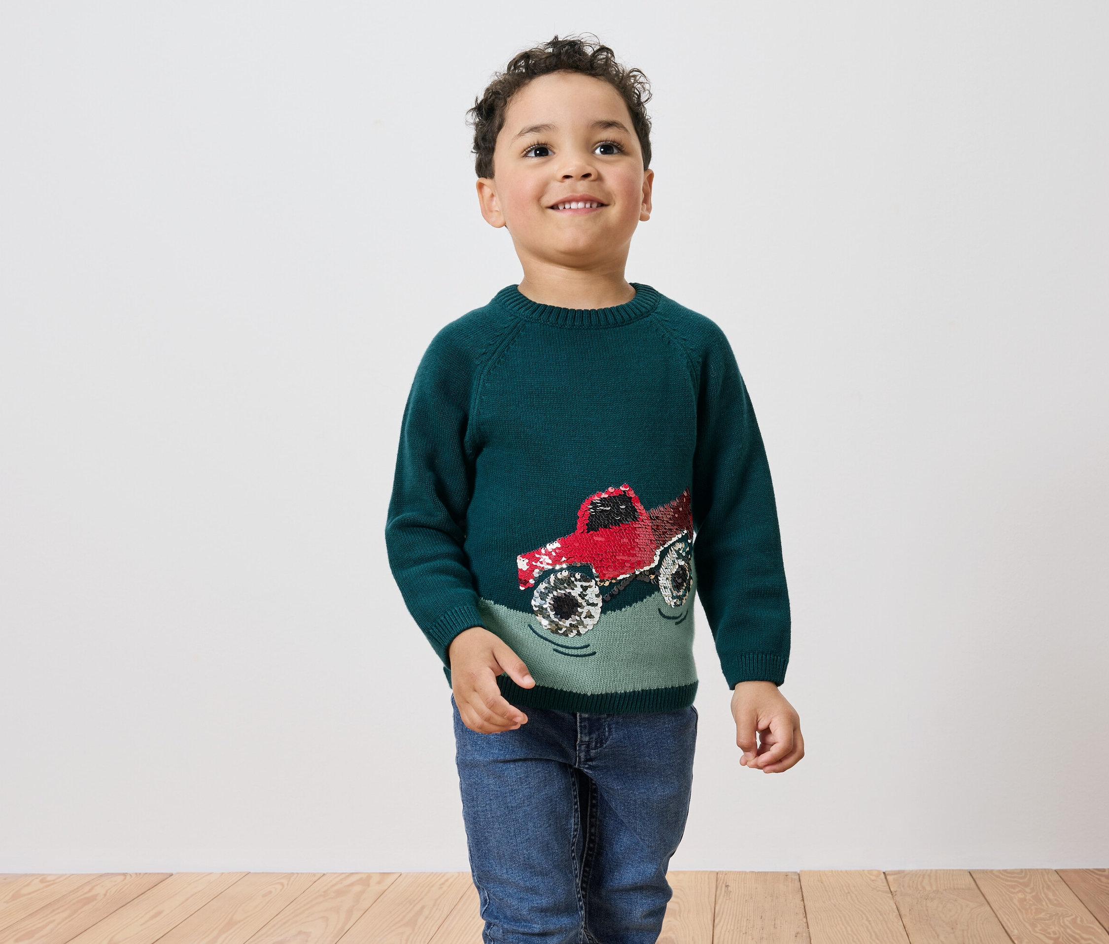 Junge trägt grünen Pullover mit rotem Monstertruck.
