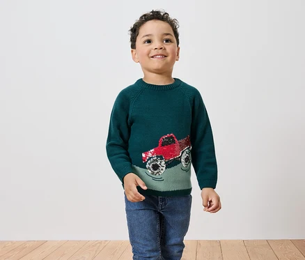 Junge trägt grünen Pullover mit rotem Monstertruck.