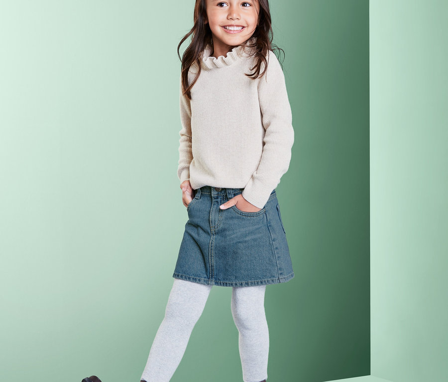 Ein lächelndes Mädchen posiert in einem Jeansrock.