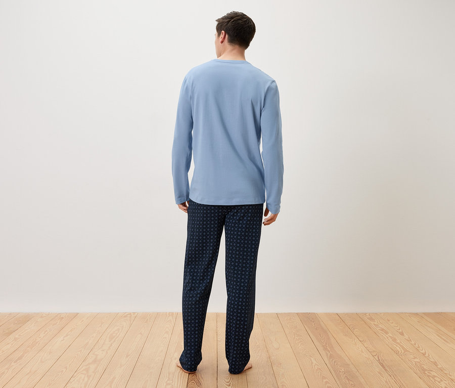 Ein Mann von hinten, der einen hellblauen Schlafanzug und eine dunkelblaue Hose trägt.