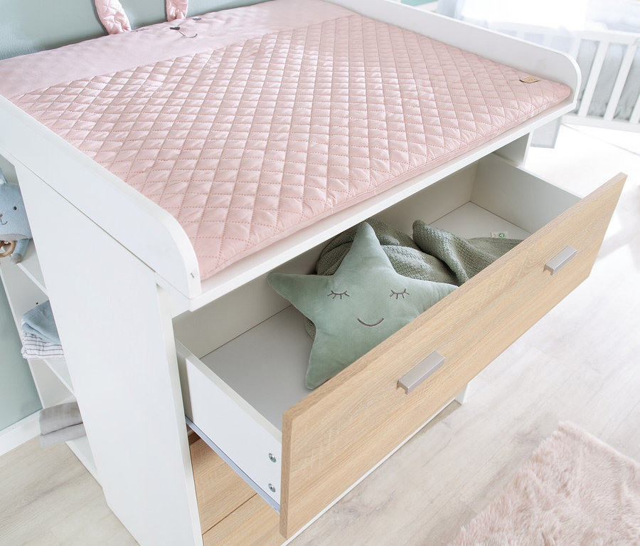 Detailansicht einer weißen Wickelkommode mit offener Schublade. In der Schublade befinden sich ein grüner Stern und eine Decke.