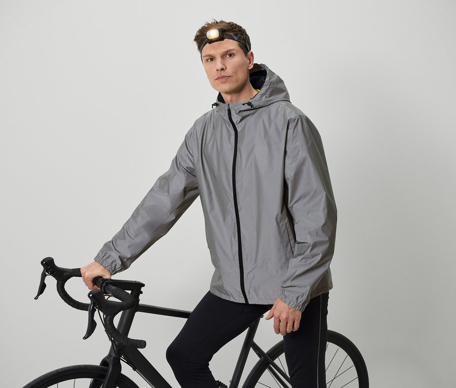 Mann mit Stirnlampe posiert mit Fahrrad in grauer Jacke.