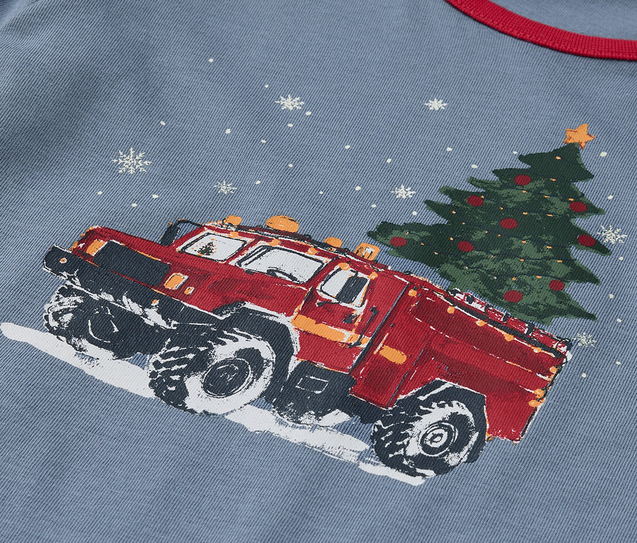 Detailaufnahme eines blauen T-Shirts mit dem Aufdruck eines roten Lastwagens, der einen Weihnachtsbaum transportiert.